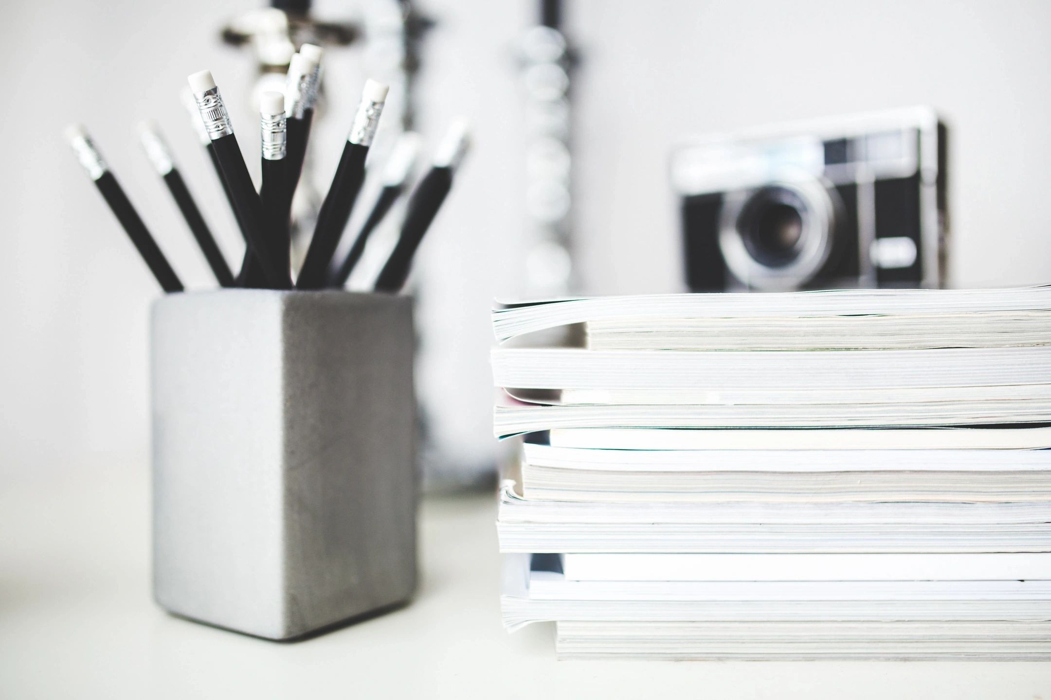 Pencils in a pot next to a camera on a pile of books